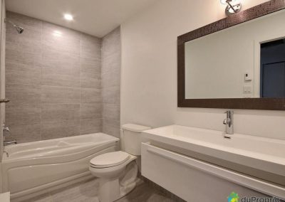 Cette salle de bain aux lignes épurées a été optimisée en utilisant la même céramique autour du bain et pour le plancher. Cette uniformité apporte une ambiance apaisante à la pièce et lui donne un aspect plus spacieux.