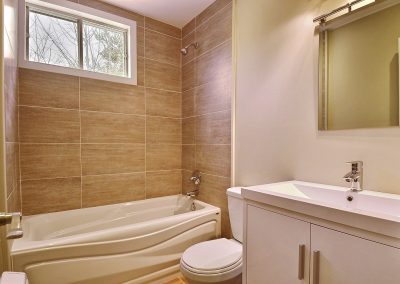 La salle de bain de grandeur modeste présente un aspect très chaleureux avec la céramique entourant le bain de couleur terre. Le nouveau bain et le nouveau meuble lavabo rendent la pièce beaucoup plus moderne.